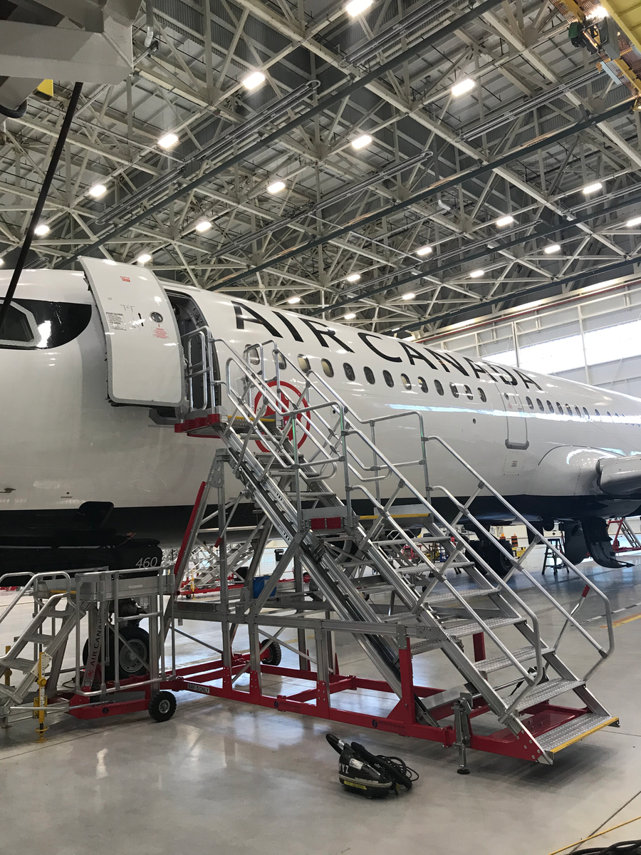 Air Canada aircraft with boarding stairs inside a steel-framed maintenance hangar